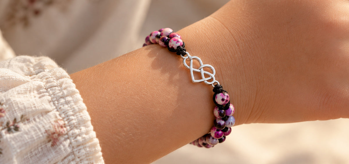 Silver infinity heart charm bracelet with pink and purple beads on a child's wrist